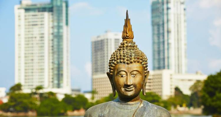 Primer plano de una serena estatua de Buda de bronce con los modernos rascacielos de Colombo desenfocados de fondo.