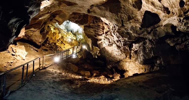 Lit walkway winding through the depths of an impressive limestone cave chamber.