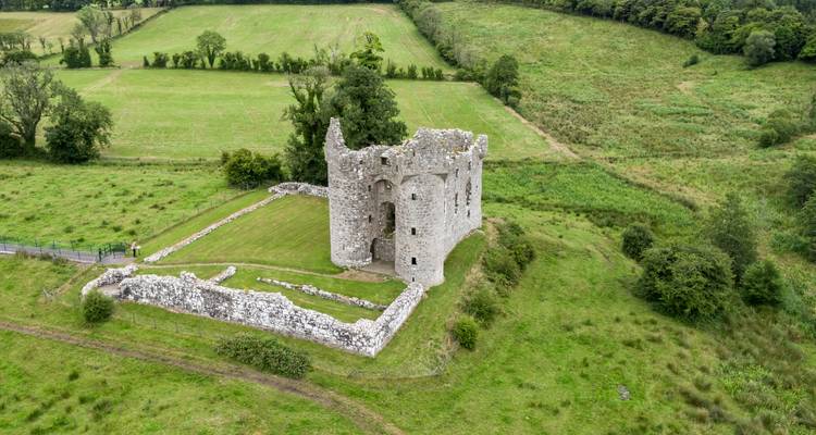 Drone view of solitary medieval stone ruin standing amid rolling green countryside.