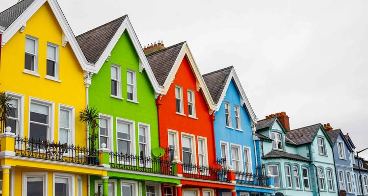 Vividly painted Victorian terrace houses with ornate railings and pointed roofs under a grey sky in coastal Ireland.