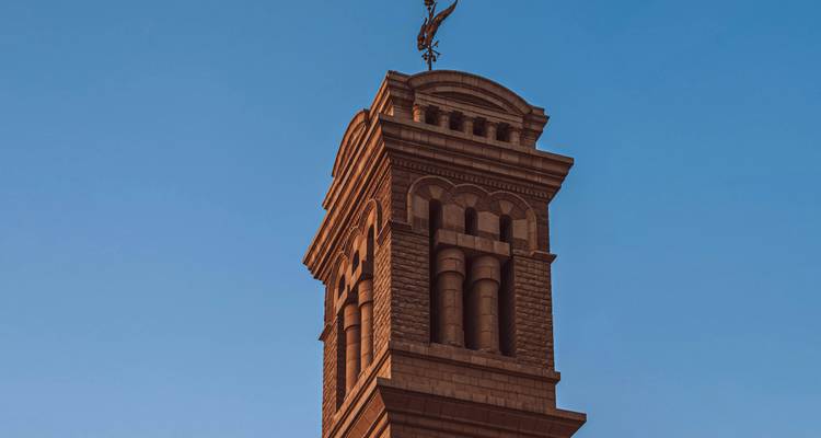 Clocher en pierre surmonté d'un ange girouette sur un ciel bleu dégagé.