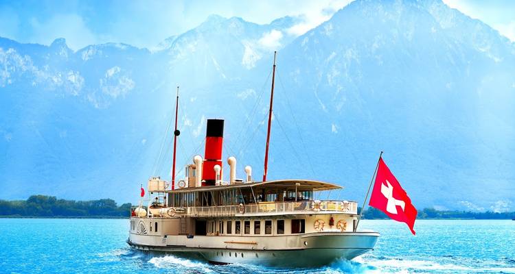Vintage paddle steamer with Swiss flag cruises across a turquoise lake backed by dramatic snow-dusted mountains.