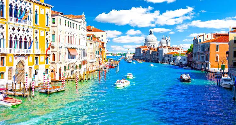 Bright Grand Canal scene with colorful palazzi, boats and the domed Santa Maria della Salute under a vivid blue sky.