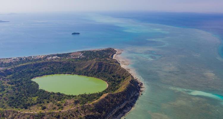 Aerial view of a green crater lake surrounded by a peninsula and turquoise ocean waters in Mayotte.