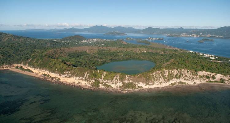 Wide aerial of a coastal crater lake with rugged shoreline and villages in the distance.