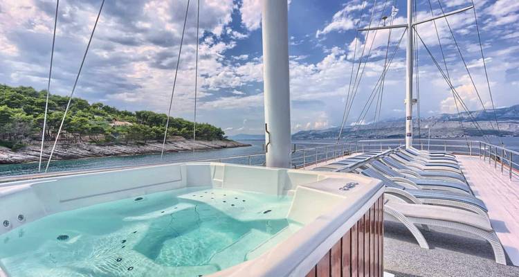 Jacuzzi op het dek met uitzicht op beboste kust en bergen met rijen zonnebedden.
