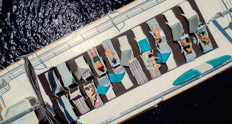Bovenaanzicht vanaf een drone van passagiers die zonnebaden op gestreepte ligstoelen op het dek van een jacht.