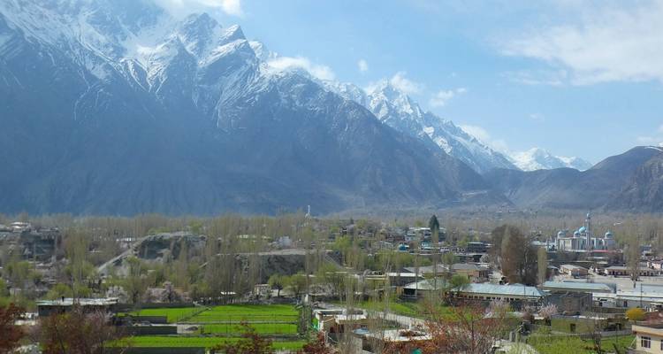 Paysage urbain de Hunza avec des champs verdoyants se détachant contre des montagnes enneigées spectaculaires sous un ciel bleu