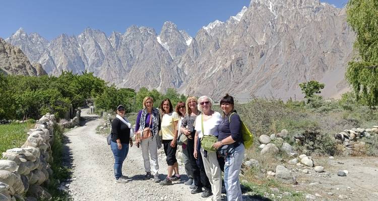 Groupe de femmes randonneuses posant sur un sentier de gravier avec les impressionnants Cônes de Passu en arrière-plan