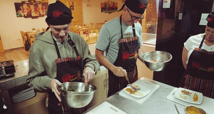 Los participantes con delantales preparan platos en la cocina de una clase de cocina.