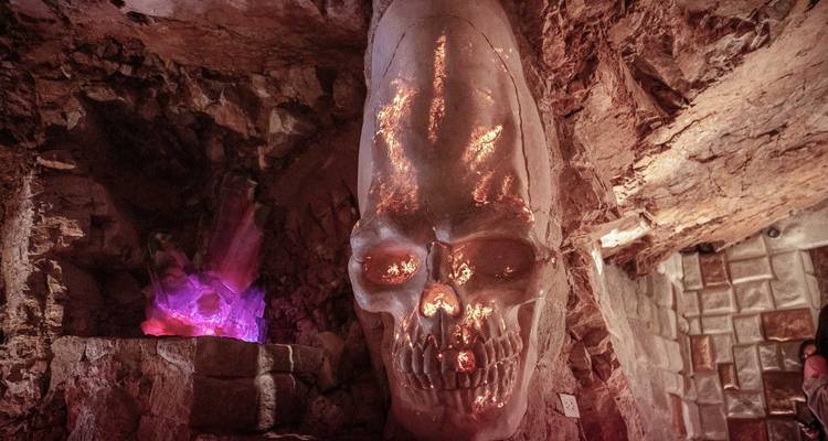 Escultura de calavera de cristal brillante en una cámara subterránea rocosa con luz violeta cerca.