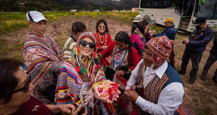Los viajeros en ponchos coloridos se ríen y muestran puñados de pétalos de flores al lado de un autobús.