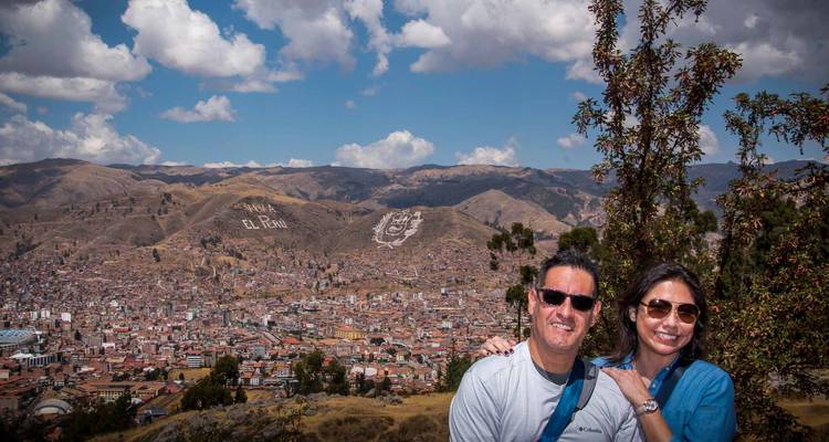 Pareja sonriente posando con la amplia vista de la ciudad de Cusco y las montañas detrás de ellos.