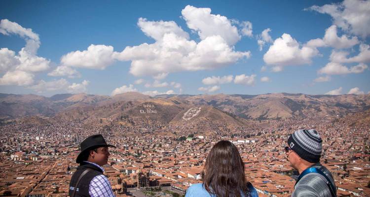 Tres viajeros conversan mientras disfrutan de la vista de los techos de terracota de Cusco desde un punto de vista en la cima de la colina.