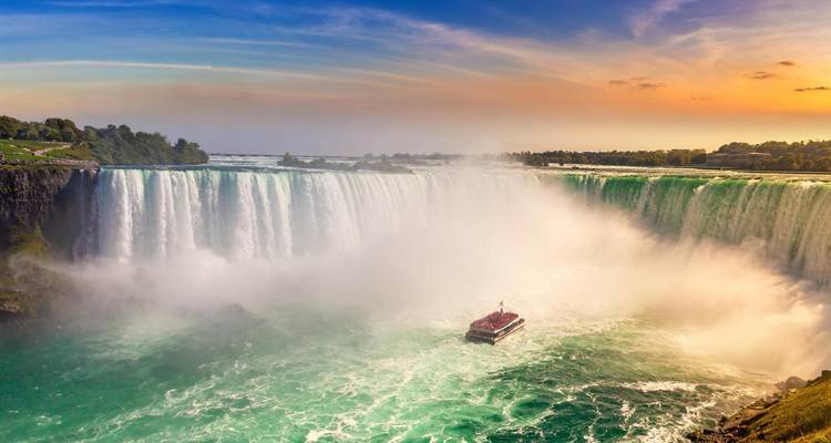 De machtige Niagara Falls stort zich in turkooizen nevel terwijl een toerboottje bij zonsondergang naar het watergordijn nadert.