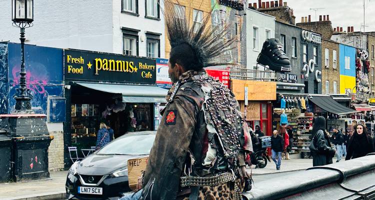 Punk met dramatische mohawk loopt langs Camden High Street met kleurrijke winkelpuien.