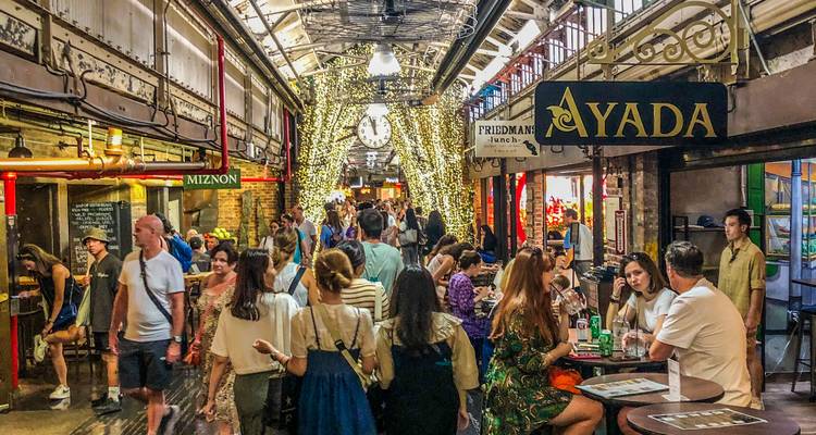 Hall gastronomique animée à l'intérieur du Chelsea Market avec des clients et des devantures de magasins alignées le long de l'allée.