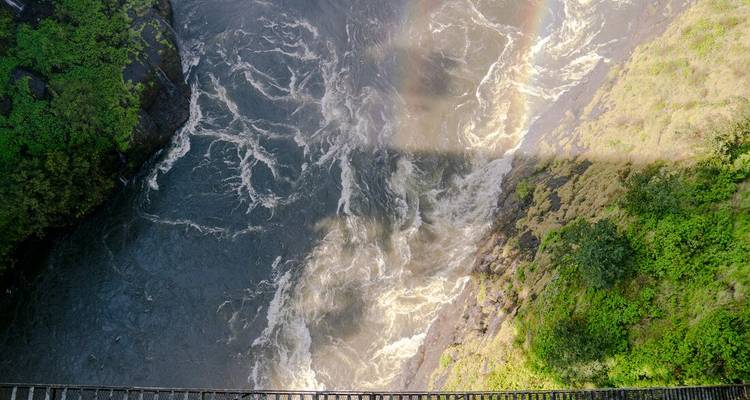 Rivier die ver beneden een brug kolkt met een dubbele regenboog die in de mist ontstaat.