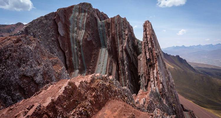 Primer plano de formaciones rocosas dentadas y dramáticas con capas de minerales vívidamente rayadas bajo cielos soleados.