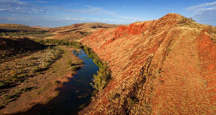 Vue aérienne d'une gorge de roche rouge et d'une rivière sinueuse brillant sous un ciel bleu dégagé.