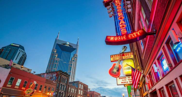 Neon-lit Broadway in Nashville featuring music bars and the iconic AT&T tower at dusk.