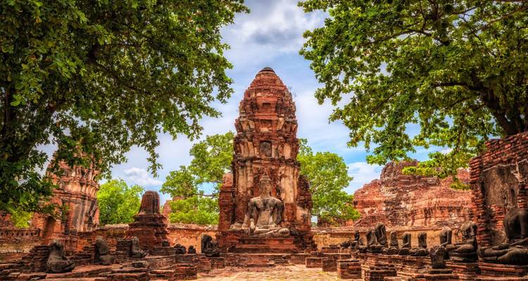 Central prang and scattered Buddha heads among Ayutthaya temple ruins framed by leafy trees.
