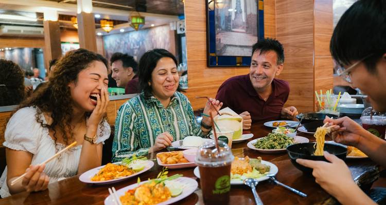Friends sharing Thai dishes and laughing together at a local Bangkok restaurant.