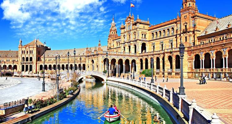 Un couple rame dans une petite embarcation le long du canal de la Plaza de España de Séville sous des arches ornées.