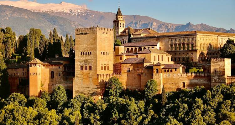 Vue baignée de soleil du complexe forteresse de l'Alhambra avec la Sierra Nevada aux sommets enneigés en arrière-plan.