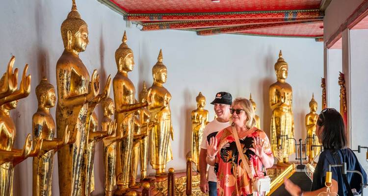 Toeristen bewonderen rijen vergulde Boeddhabeelden in een tempelhal in Bangkok.