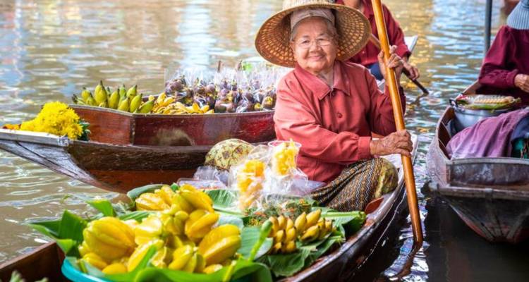 Bejaarde vrouw die glimlacht terwijl zij tropische vruchten verkoopt van een houten boot op de drijvende markt.