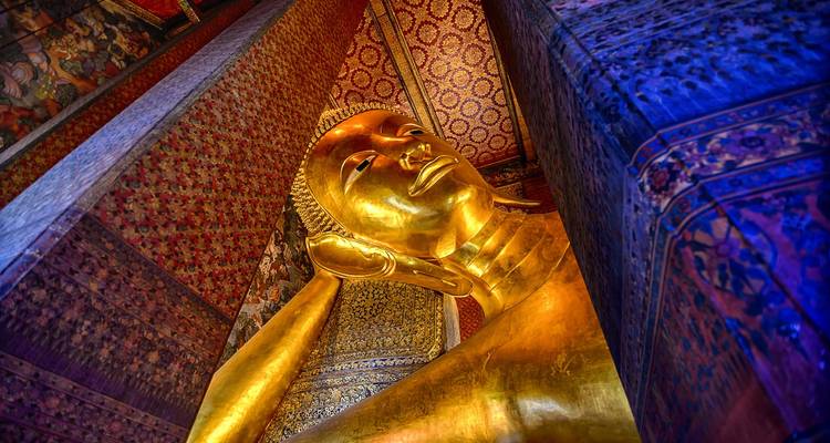 Close-up van het sereen gezicht van de gouden Liggende Boeddha en het ingewikkeld gemusterde plafond.