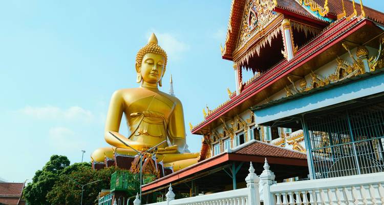 Bouddha assis en or dominant à côté de bâtiments de temple thaïlandais ornés contre le ciel bleu
