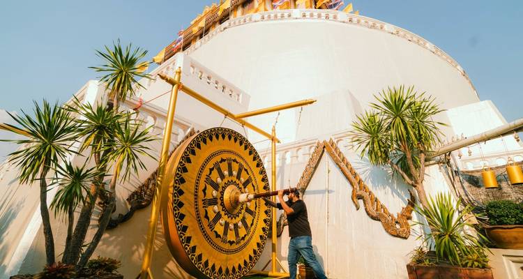 Un visiteur frappant un grand gong cérémoniel à la base de la stupa blanche de la Montagne d'Or par une journée dégagée.