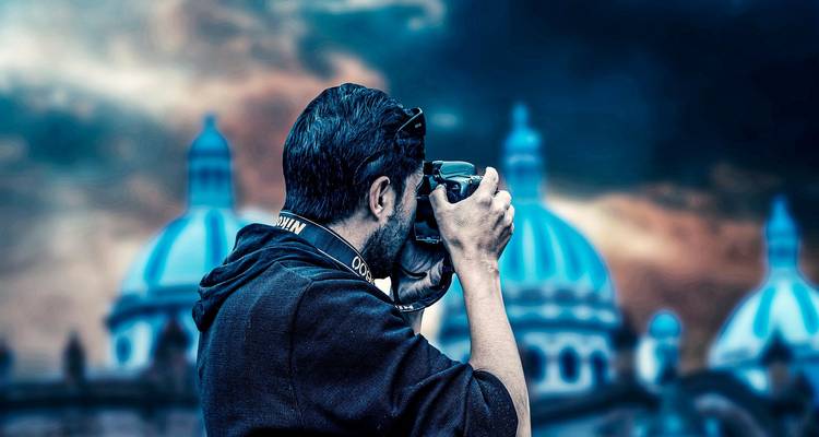 Mann, der eine DSLR-Kamera verwendet, mit unscharfem, blaugedeckeltem Dom im Hintergrund während eines düsteren Himmels.