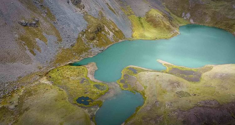 Drone-perspectief van een turquoise alpien meer en kleine aangrenzende poelen nesteld in ruige bergen.