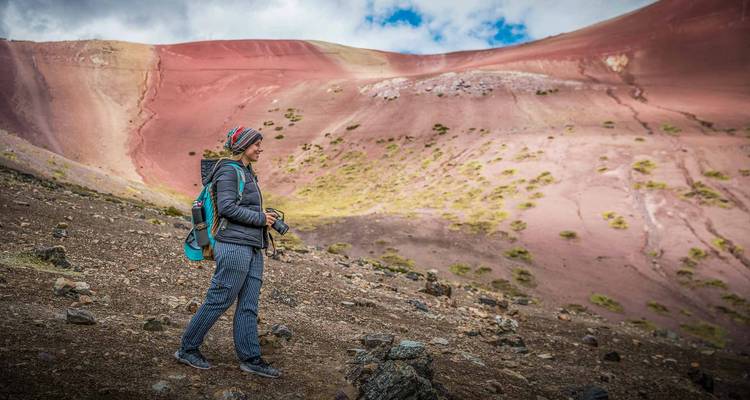 Vrouwelijke reiziger met rugzak kijkt uit over de pastelkleurige hellingen van het Rainbow Mountain-gebergte.