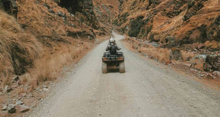 Een ATV-rijder reist alleen over een stoffige bergweg naast een rivierkloofje.