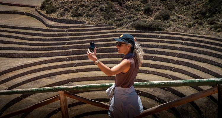 Vrouw die een telefoonfoto maakt van de concentrische terrassen van Moray vanaf een houten uitkijkpunt
