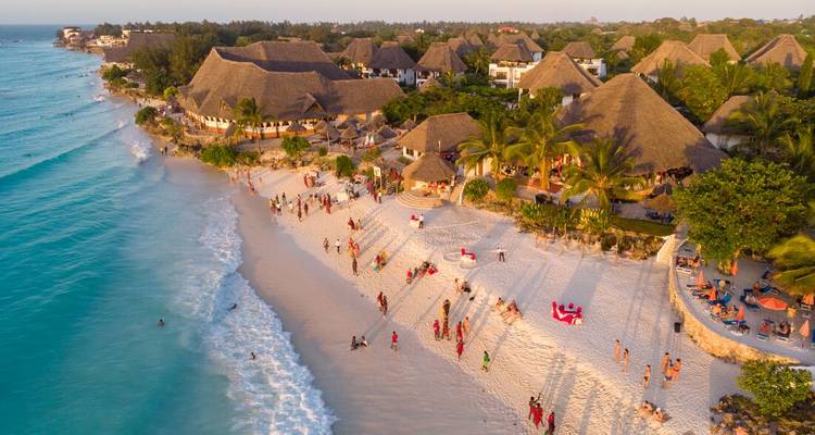Luftaufnahme eines belebten Strandes mit weißem Sand und Resorts entlang türkisfarbenem Wasser auf einer tropischen Insel