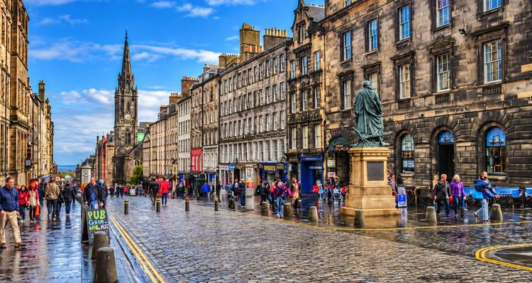 La célèbre Royal Mile d'Édimbourg, animée et bordée de bâtiments historiques en pierre, avec un clocher d'église et des pavés mouillés après la pluie.