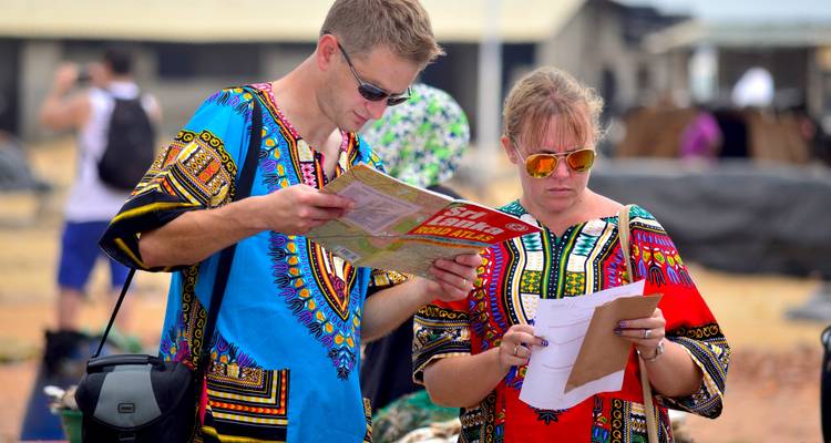 Twee reizigers in levendige shirts bestuderen een kaart en aantekeningen op een buitenmarkt.