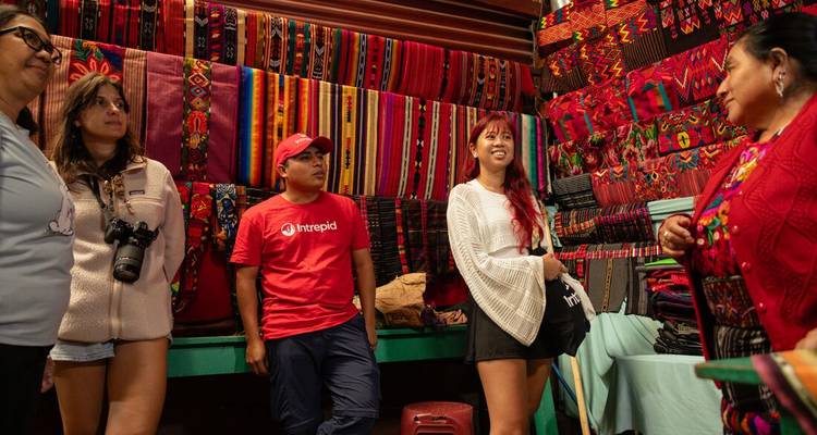 Les voyageurs discutent avec un artisan local entouré de textiles tissés aux couleurs éclatantes.