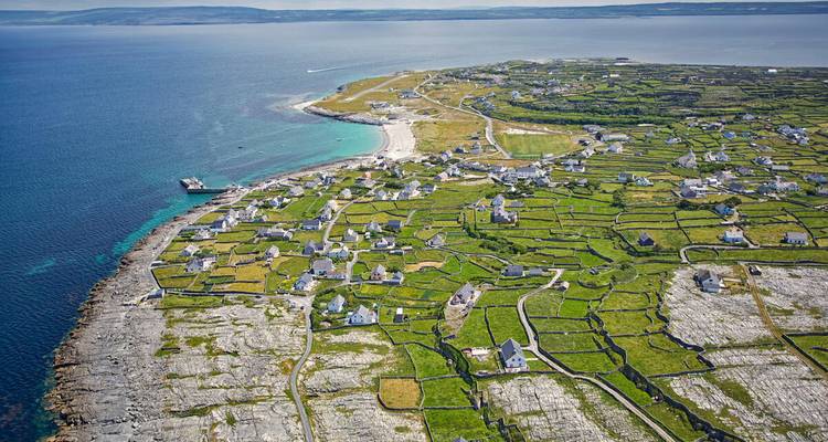 Vue aérienne de champs aux murs de pierre et de petits cottages blancs sur une île d'Aran qui s'avance dans une mer bleu éclatant.