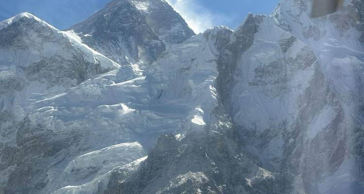 Dicht luchtfoto van de ijzige top van Mount Everest en glaciaal uitgehouwen bergkammen onder een heldere hemel.