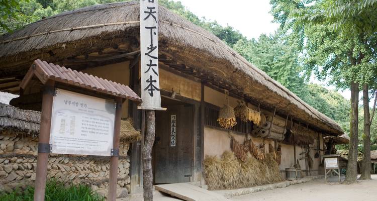 Maison paysanne traditionnelle coréenne avec toit de chaume et cultures suspendues dans un village folklorique.