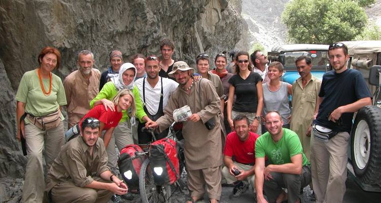 Large trekking group poses with loaded bicycles in a rocky canyon beside jeeps.