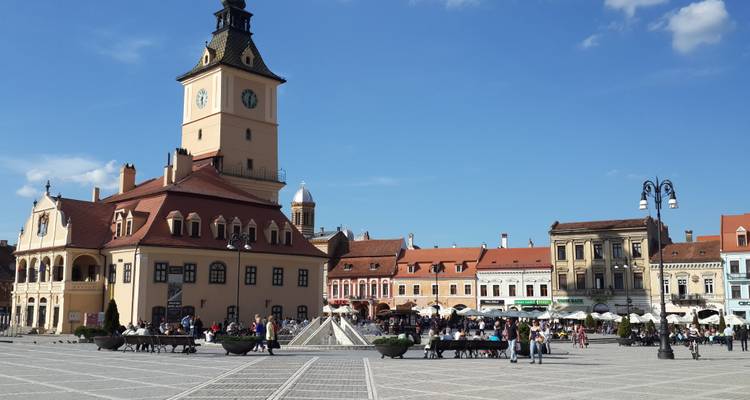 Place principale animée à Brașov avec la maison du conseil historique et la tour de l'horloge, bordée de bâtiments baroques colorés et de foules de visiteurs.