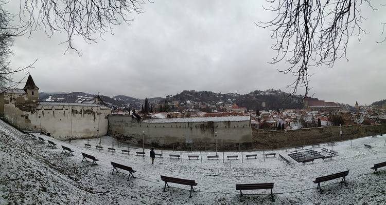 Les murs défensifs saupoudrés de neige surplombant les toits de Brasov et les collines environnantes lors d'une journée d'hiver grise.