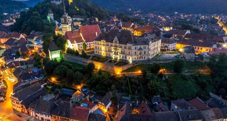 Luchtfoto 's nachts van Sighisoara's verlichte citadel en de lichjes van de omliggende stad.